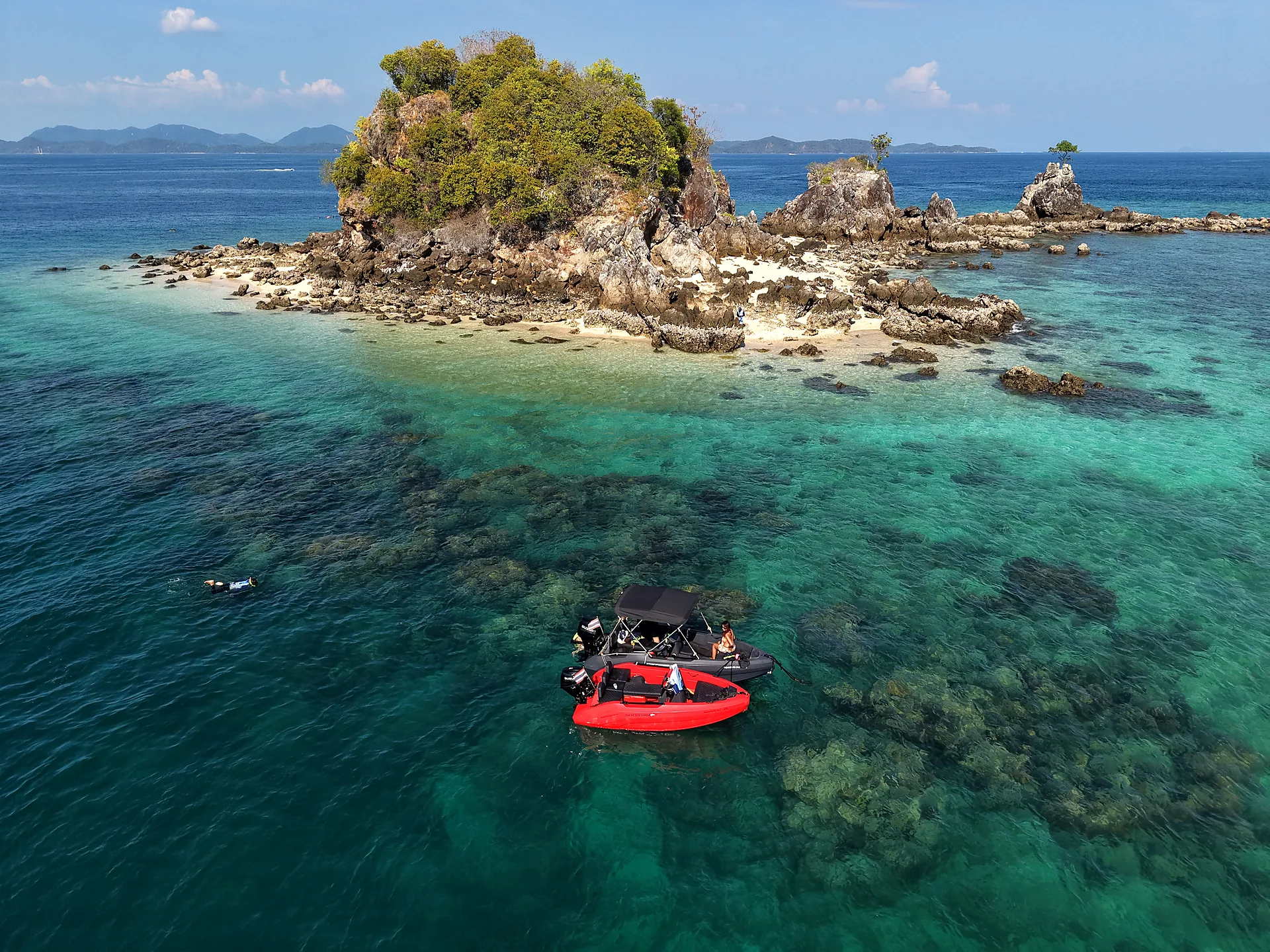 Aerial view of a mini speedboat anchored at a small rocky island with clear water and coral